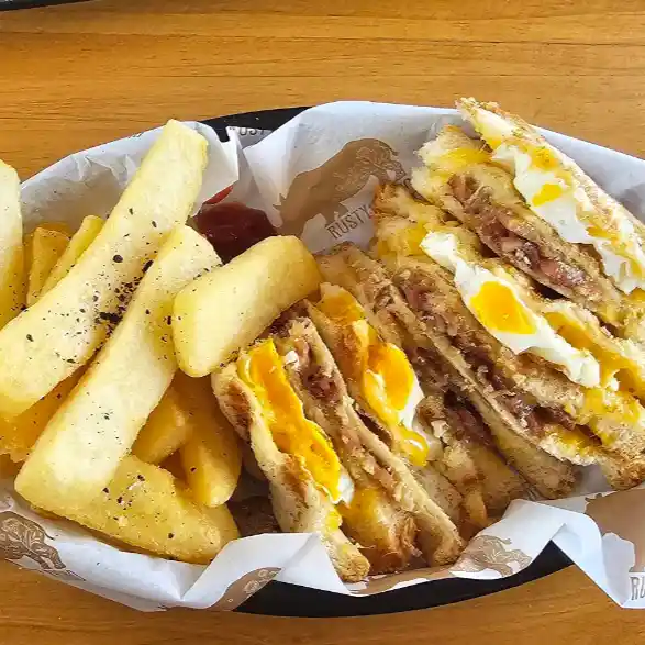 An egg and bacon toasted sandwich with chips.